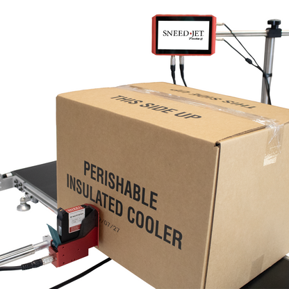 Angled view of SNEEDJET Freedom 22 controller and print head marking a moving cardboard box on a conveyor