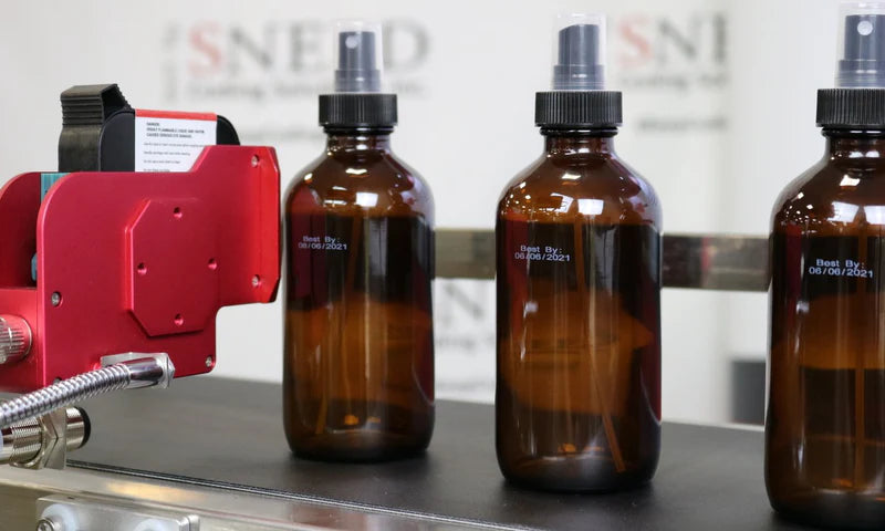 White ink best-by date printed on amber glass bottles during a SNEED-JET Titan coding demonstration